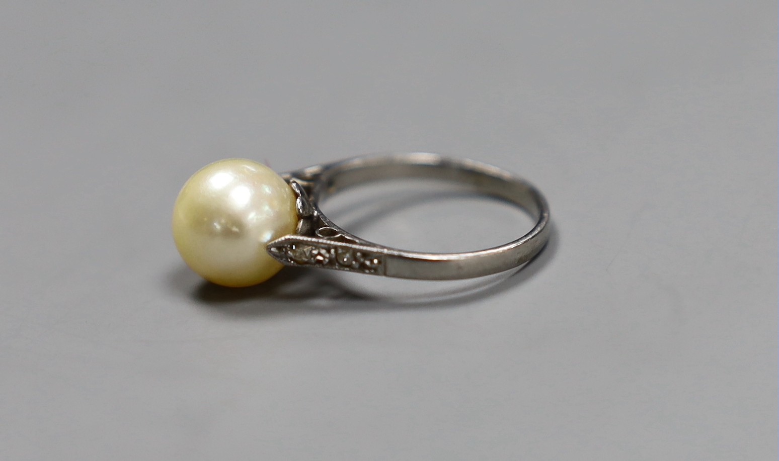 A solitaire cultured pearl set ring, with diamond chip set shoulders, size K